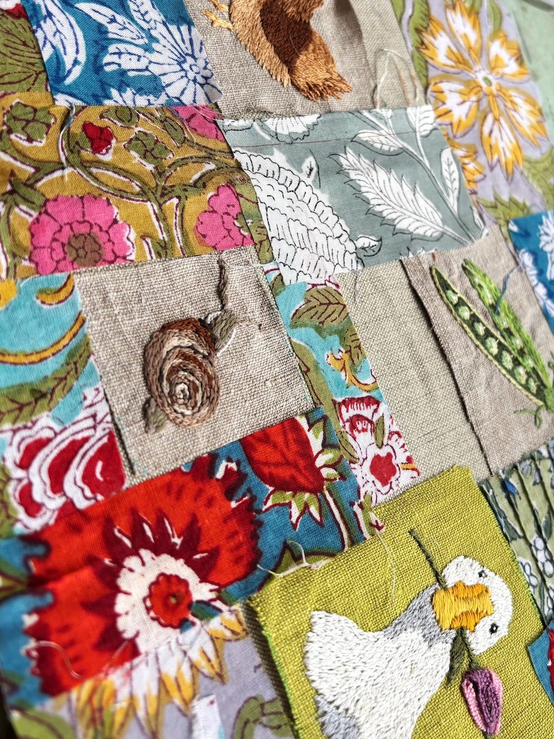 May include: A patchwork textile featuring squares of floral patterned fabric in red, yellow, blue, and green, interspersed with plain linen squares. Embroidered details include a brown snail, a green pea pod, and a white goose holding a flower.