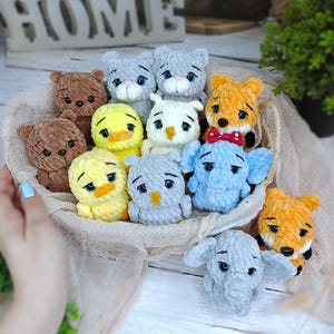 May include: A collection of handmade crochet animal toys, including bears, cats, ducks, owls, foxes, and elephants. The toys are in a woven basket, with a neutral-colored fabric. The animals have detailed features and are in various colors.