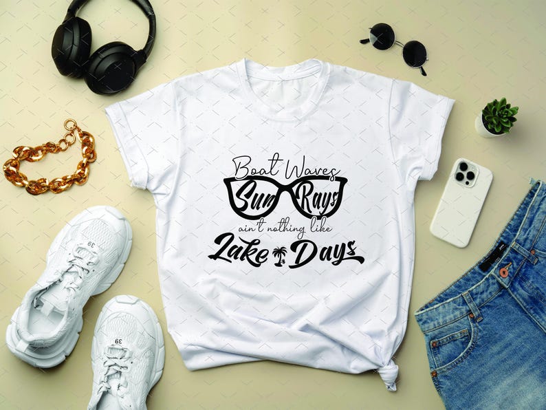 May include: White t-shirt with the text "Boat Waves, Sun Rays, ain't nothing like Lake Days" in black. The shirt is surrounded by accessories including white sneakers, a gold chain bracelet, black headphones, sunglasses, a phone, and denim shorts.