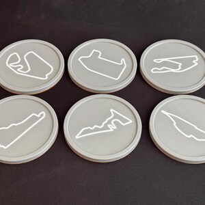 Puede incluir: Seis posavasos redondos grises con contornos blancos de diferentes circuitos de carreras. Los posavasos est&aacute;n hechos de un material liso y duradero y son perfectos para proteger las superficies de derrames y ara&ntilde;azos.