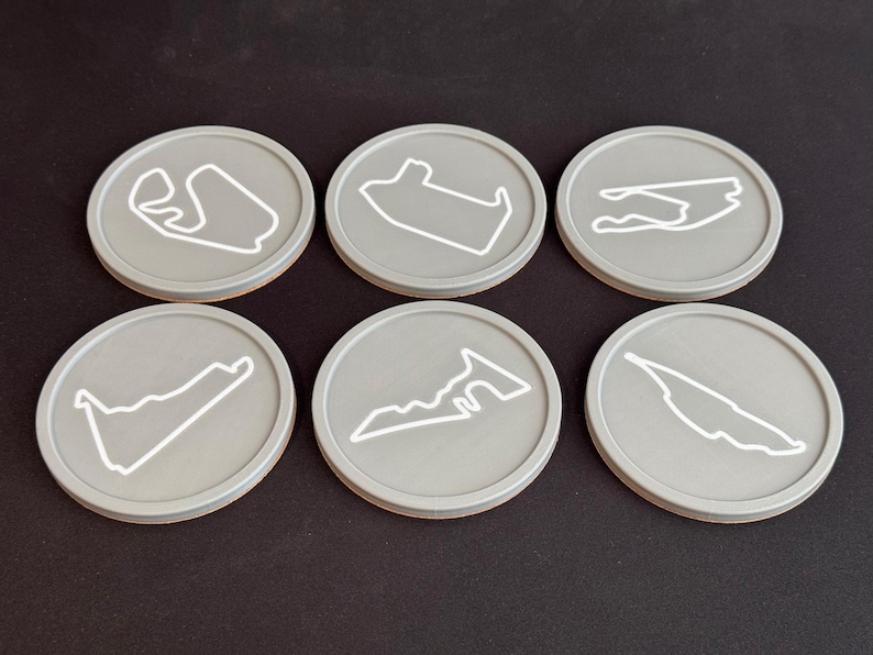 Puede incluir: Seis posavasos redondos grises con contornos blancos de diferentes circuitos de carreras. Los posavasos est&aacute;n hechos de un material liso y duradero y son perfectos para proteger las superficies de derrames y ara&ntilde;azos.