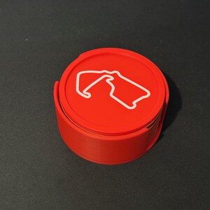 Puede incluir: Un juego de posavasos rojos con un contorno blanco de una pista de carreras. Los posavasos est&aacute;n apilados uno encima del otro.