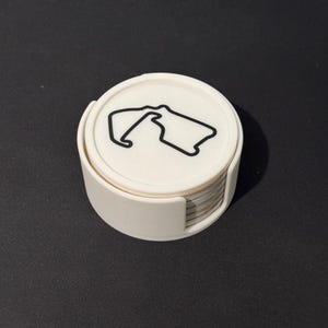 Puede incluir: Un conjunto de posavasos blancos con un contorno negro de un circuito de carreras en el posavasos superior.