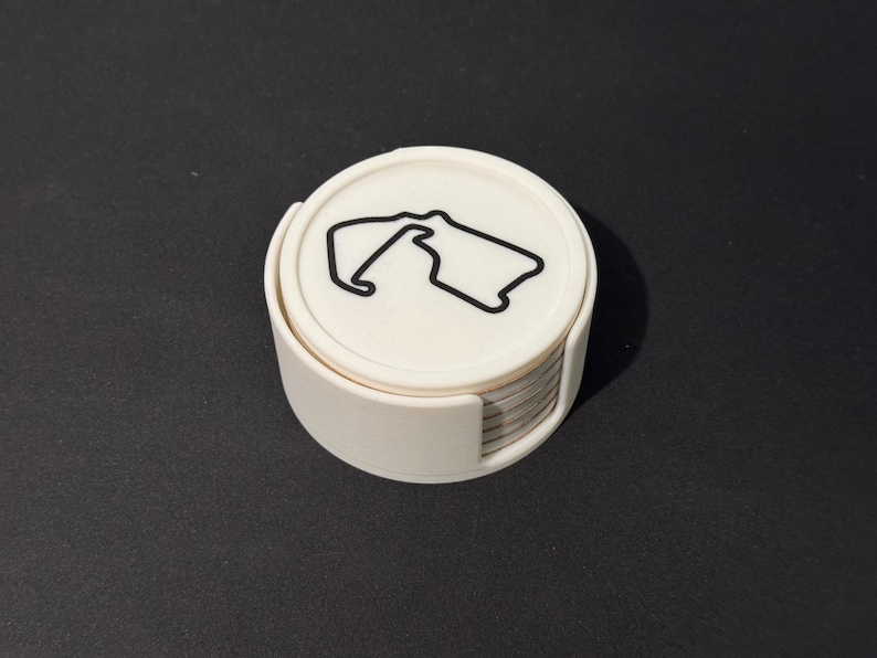Puede incluir: Un conjunto de posavasos blancos con un contorno negro de un circuito de carreras en el posavasos superior.