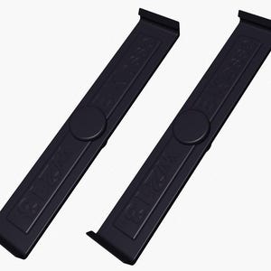 Puede incluir: Dos objetos negros rectangulares con extremos redondeados y un botón circular en el centro. Los objetos tienen el texto "SEESAW" y "W213" en relieve. Los objetos están inclinados uno hacia el otro sobre un fondo blanco.