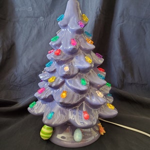 May include: A purple ceramic Easter tree with colorful lights and egg ornaments. The tree is decorated with a yellow and orange striped egg on top.