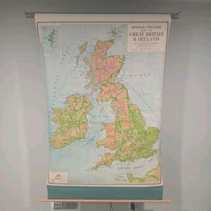 May include: A large, vintage-style wall-mounted pull-down map titled Physical Political Map of Great Britain & Ireland. The map features detailed topography in shades of green and tan, with blue oceans, mounted on wooden rollers with a teal bottom border.