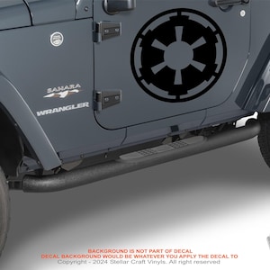 May include: A gray Jeep Wrangler Sahara with a black Imperial Star Wars logo decal on the driver's side door. The Jeep has black side steps and black wheels.