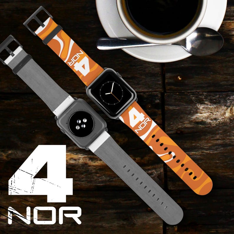 May include: Two smart watch bands are displayed. One is gray, the other is orange with a white and orange wave pattern. Both bands have the text "4 NOR" printed on them. A cup of coffee and a spoon are in the background.