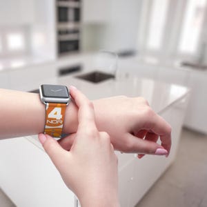 May include: A silver smartwatch with a colorful band featuring the number 4 and the letters NOR in white. The band has an orange and yellow gradient design. The watch is being touched by a person's fingers.