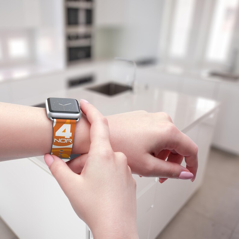 May include: A silver smartwatch with a colorful band featuring the number 4 and the letters NOR in white. The band has an orange and yellow gradient design. The watch is being touched by a person's fingers.