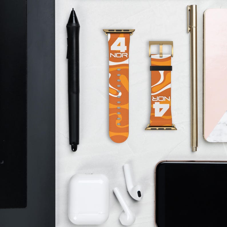 Könnte beinhalten: Orange und weiß gemusterte Uhrenarmbänder mit goldfarbener Hardware. Die Armbänder zeigen den Text "4 NOR" in Weiß. Ein schwarzer Stift, ein goldener Stift und kabellose Ohrhörer sind ebenfalls sichtbar.