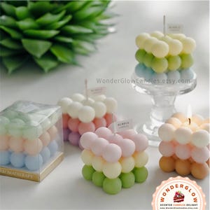 May include: Four colorful bubble candles in various shades of green, pink, yellow, and blue. The candles are stacked in a square shape and have a textured bubble design. The candles are labeled "Bubble Candles" and "Aromatherapy".