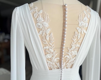 May include: White wedding dress with long sleeves and a lace back detail. The dress has a fitted bodice and a flowing skirt.