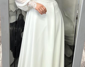 May include: A white wedding dress with a V-neckline and long sleeves. The sleeves are made of sheer fabric with lace detailing at the cuffs. The dress has a fitted bodice and a flowing skirt.