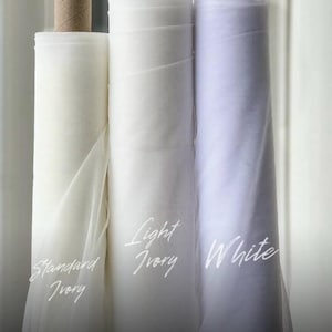 Puede incluir: Tres rollos de tela en diferentes tonos de blanco. El rollo de la izquierda está etiquetado como "Standard Ivory", el rollo del medio está etiquetado como "Light Ivory" y el rollo de la derecha está etiquetado como "White".