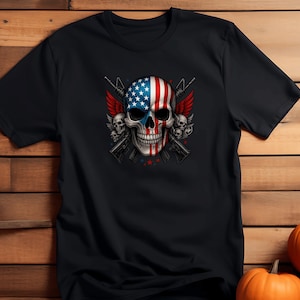 May include: Black t-shirt featuring a skull design with an American flag motif. The skull has red and white stripes and blue stars. Two rifles and red wings are behind the skull. The shirt is on a wooden background with pumpkins.