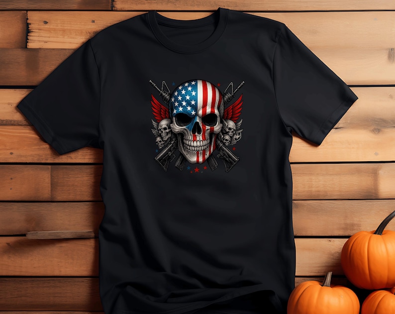 May include: Black t-shirt featuring a skull design with an American flag motif. The skull has red and white stripes and blue stars. Two rifles and red wings are behind the skull. The shirt is on a wooden background with pumpkins.
