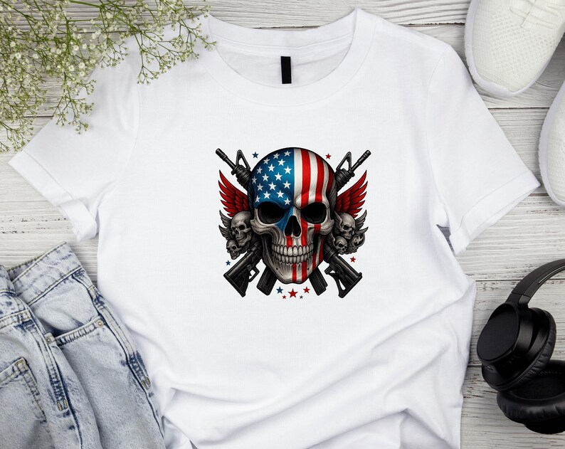 May include: White t-shirt featuring a skull design with an American flag motif. The skull has a blue and white stars and stripes pattern, with red wings and two rifles crossed behind it. The design includes red stars.