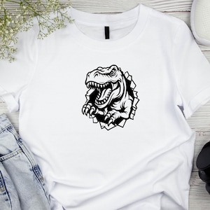 May include: White t-shirt featuring a black graphic of a dinosaur breaking through a wall.
