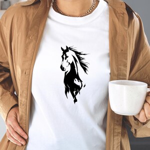May include: White t-shirt featuring a black and white graphic of a horse. The horse is depicted in a stylized, flowing design. The shirt is made of a soft material and is suitable for casual wear.