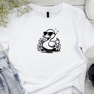 May include: White t-shirt with a black graphic of a duck wearing sunglasses and floating in water with flowers.