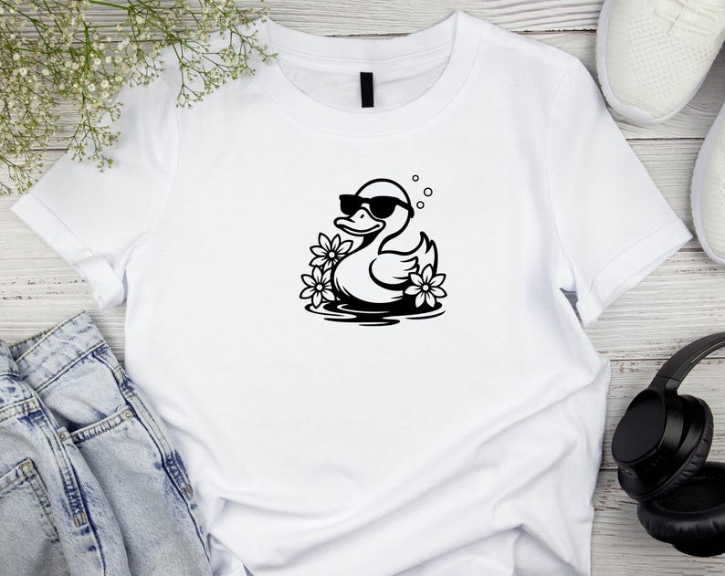 May include: White t-shirt with a black graphic of a duck wearing sunglasses and floating in water with flowers.