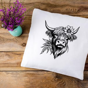 May include: A white pillow with a black and white illustration of a Highland cow with a flower in its hair.