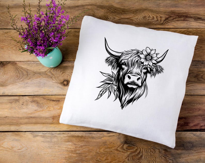 May include: A white pillow with a black and white illustration of a Highland cow with a flower in its hair.