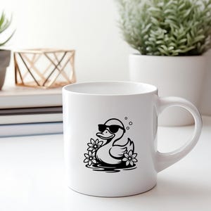 May include: White ceramic mug with a black and white illustration of a duck wearing sunglasses and floating in water with flowers.