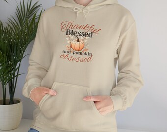 May include: A beige hoodie with a graphic print of a pumpkin and the text "Thankful Blessed and pumpkin obsessed".