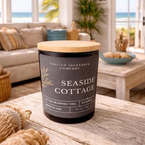 May include: A black candle with a wooden lid, labeled "Seaside Cottage" by Vaulted Treasures Company. The candle is 12 oz / 355 ml and made in the USA. The candle has a 40-hour burning time.