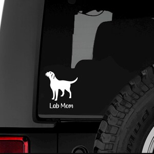 Puede incluir: Calcomanía de vinilo blanco con la silueta de un Labrador Retriever sobre un fondo negro con el texto "Lab Mom" debajo. La calcomanía está en la ventana trasera de un SUV negro.