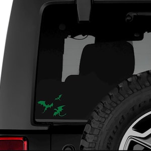 May include: A black car with a green dragon decal on the back window. The dragon is facing to the right and has its wings spread out.