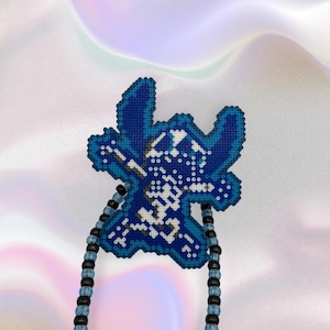 Pode incluir: Pingente pixelizado Stitch azul e branco com um colar de contas. O pingente &eacute; um design de ponto cruz detalhado, com tons de azul e branco. O colar tem contas pretas e azuis alternadas.