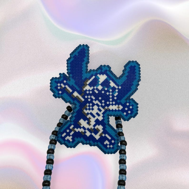 Pode incluir: Pingente pixelizado Stitch azul e branco com um colar de contas. O pingente &eacute; um design de ponto cruz detalhado, com tons de azul e branco. O colar tem contas pretas e azuis alternadas.
