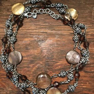 May include: A multi-strand necklace with brown and gold shell beads, silver chain links, and brown crystal beads.