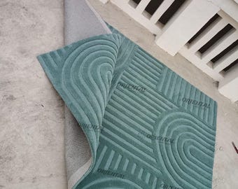 May include: A teal blue rug with a geometric pattern of curved lines and stripes. The rug is rolled up on one side, revealing the gray backing. The text "ORIENTAL" is printed on the rug.