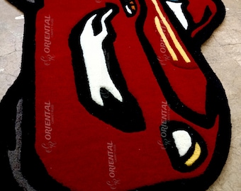 May include: Red, black and white cartoon rug depicting a car with a large, toothy grin. The rug is made of a soft, plush material and has a black border.