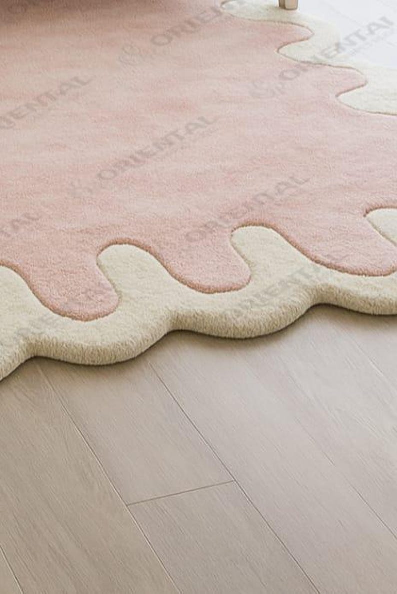 Modern abstract scalloped edge pink rug in size 8x10 ft, styled with white bedding, natural wood flooring and indoor greenery Luxurious hand tufted blush pink rug with cream wave border, 6x9 ft, styled in a cozy minimalist bedroom with natural light and soft tones.
