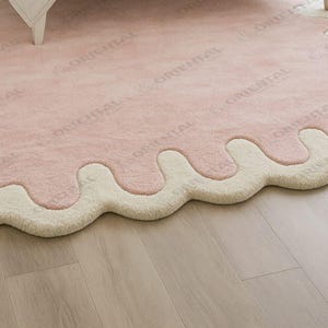 Modern scalloped edge rug 4x6 ft in pastel pink under bed Handmade wool rug 6x9 ft with cream border in bright bedroom.