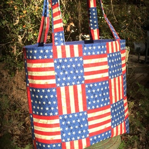 Könnte beinhalten: Eine rot-weiß-blaue Tragetasche mit einem Patchwork-Muster aus amerikanischen Flaggen. Die Tasche hat zwei Henkel und ist aus Stoff.