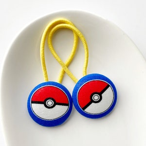 May include: Two yellow hair ties with blue and red Pokeball buttons.
