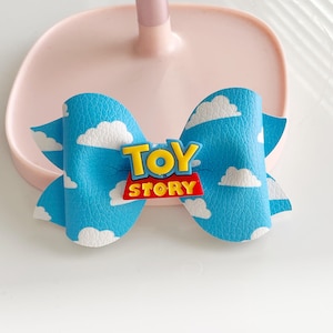 May include: A blue and white bow with a red and yellow "Toy Story" logo. The bow has a white cloud pattern.