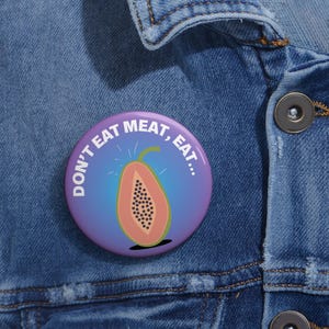 Puede incluir: Un botón morado y azul con el texto "Don't Eat Meat, Eat..." y una ilustración de papaya.