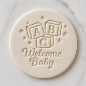 Può includere: Tagliapasta rotondo color crema chiaro con la scritta "Welcome Baby" in corsivo. Sopra il testo, tre blocchi dell'alfabeto con le lettere A, B e C e piccole stelle. Ideale per biscotti per baby shower.