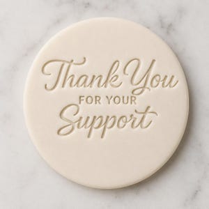 Op de afbeelding: Een rond, crèmekleurig object met de woorden "Thank You For Your Support" in sierlijke letters gegraveerd. Het object heeft een glad oppervlak en een eenvoudig ontwerp.