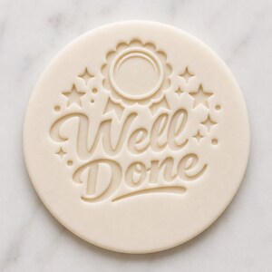 May include: A circular, cream-coloured cookie stamp with the words "Well Done" in elegant script. The design includes a ribbon motif and star embellishments, ideal for baking and crafting projects. The stamp is perfect for creating decorative cookies.