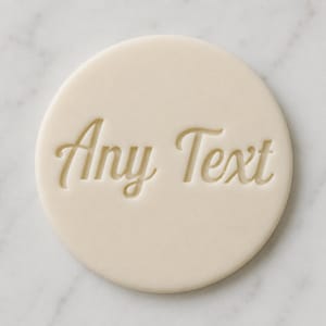 May include: A circular, pale-cream cookie or stamp with the words "Any Text" embossed in a cursive font. The text is centrally positioned on the circular surface, offering a simple and elegant design.
