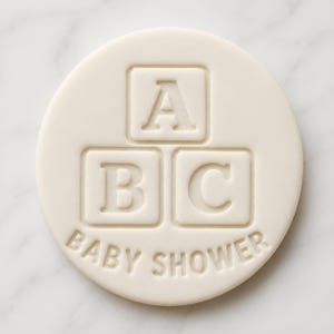 Può includere: Decorazione rotonda color crema per baby shower con le lettere "A", "B" e "C" in blocchi quadrati. Le parole "BABY SHOWER" sono incise sul bordo. Il design è in rilievo.